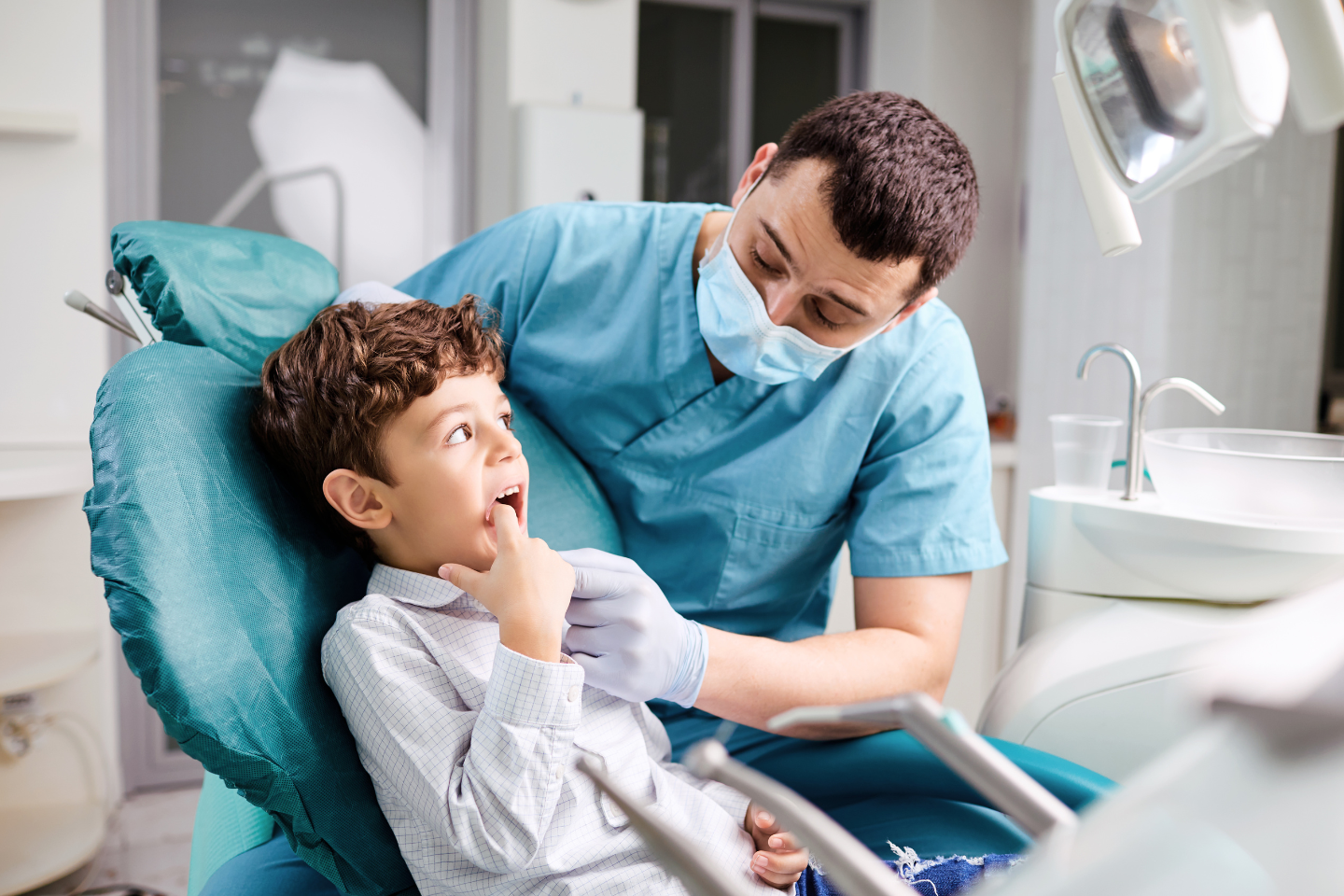 Child smiling happily in a dental chair with pediatric dentist gently examining teeth.
