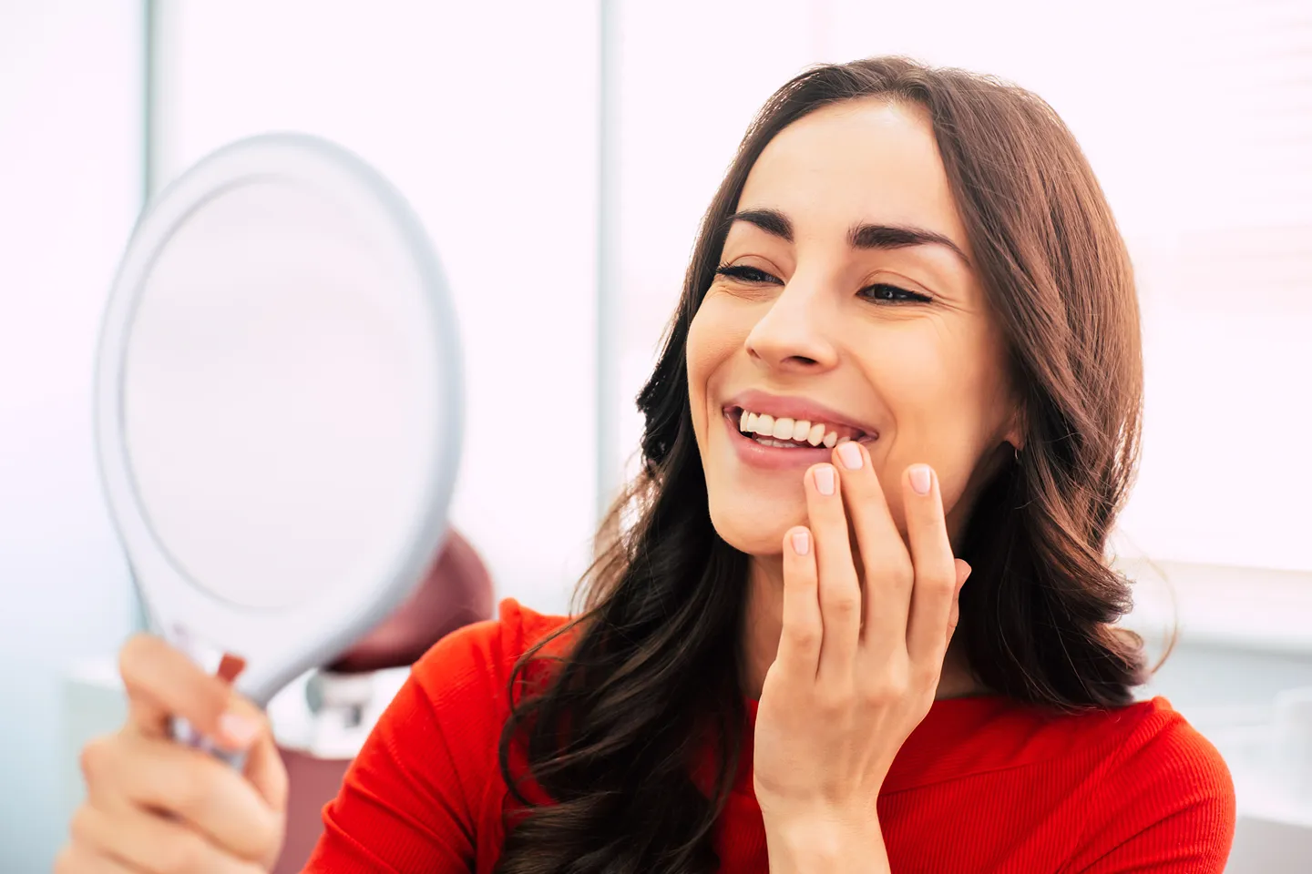 Smiling adult examining teeth in mirror—symbolizes satisfaction with long-lasting dental implants in Malden, MA.