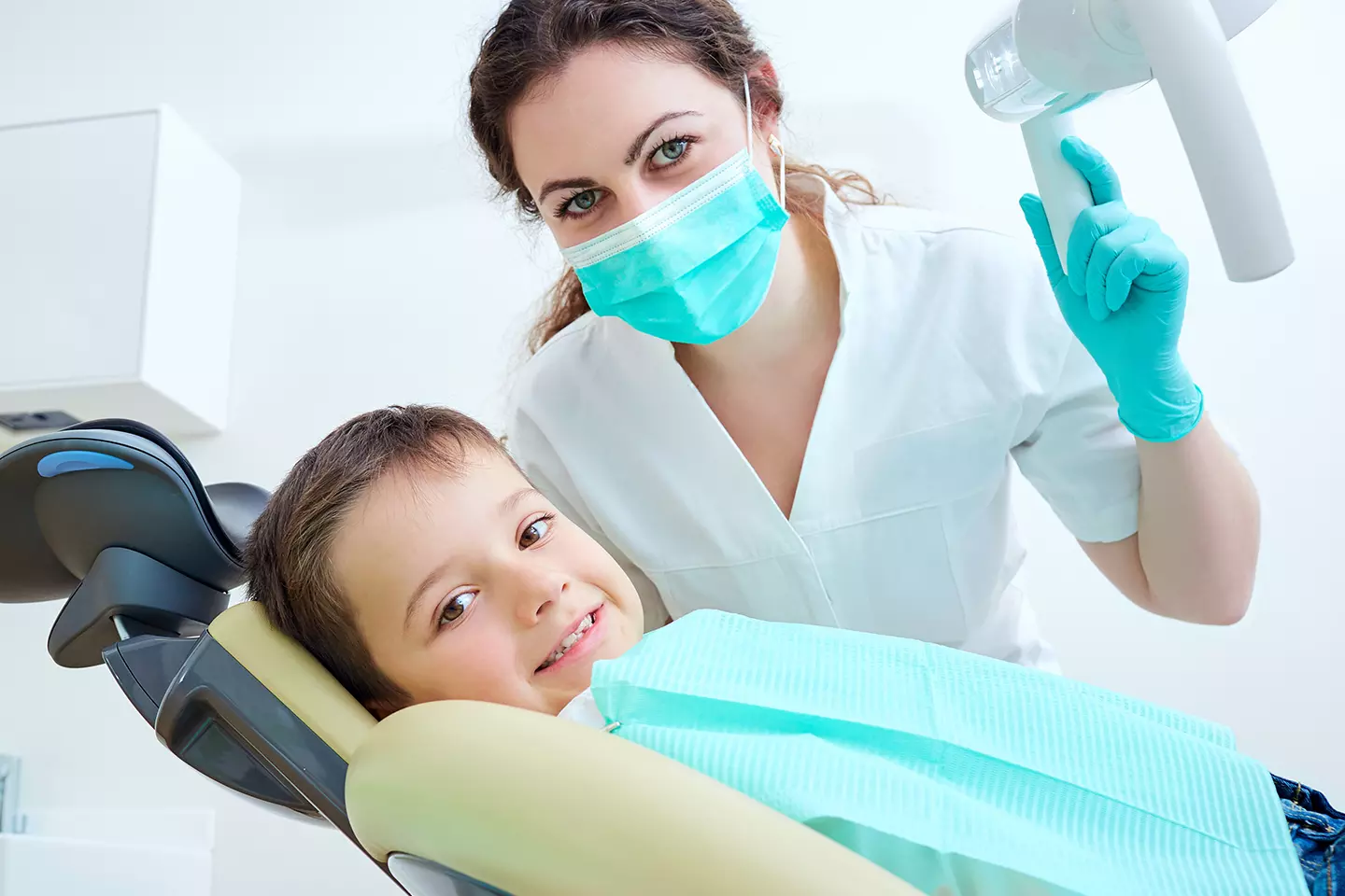 Child smiling happily in a dental chair with pediatric dentist gently examining teeth.
